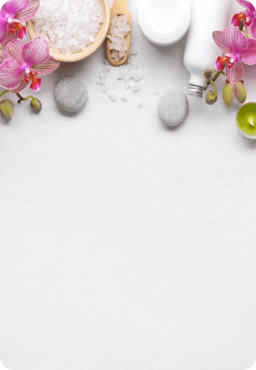 Spa essentials with pink orchids, stones, and bath salts arranged on a white surface.