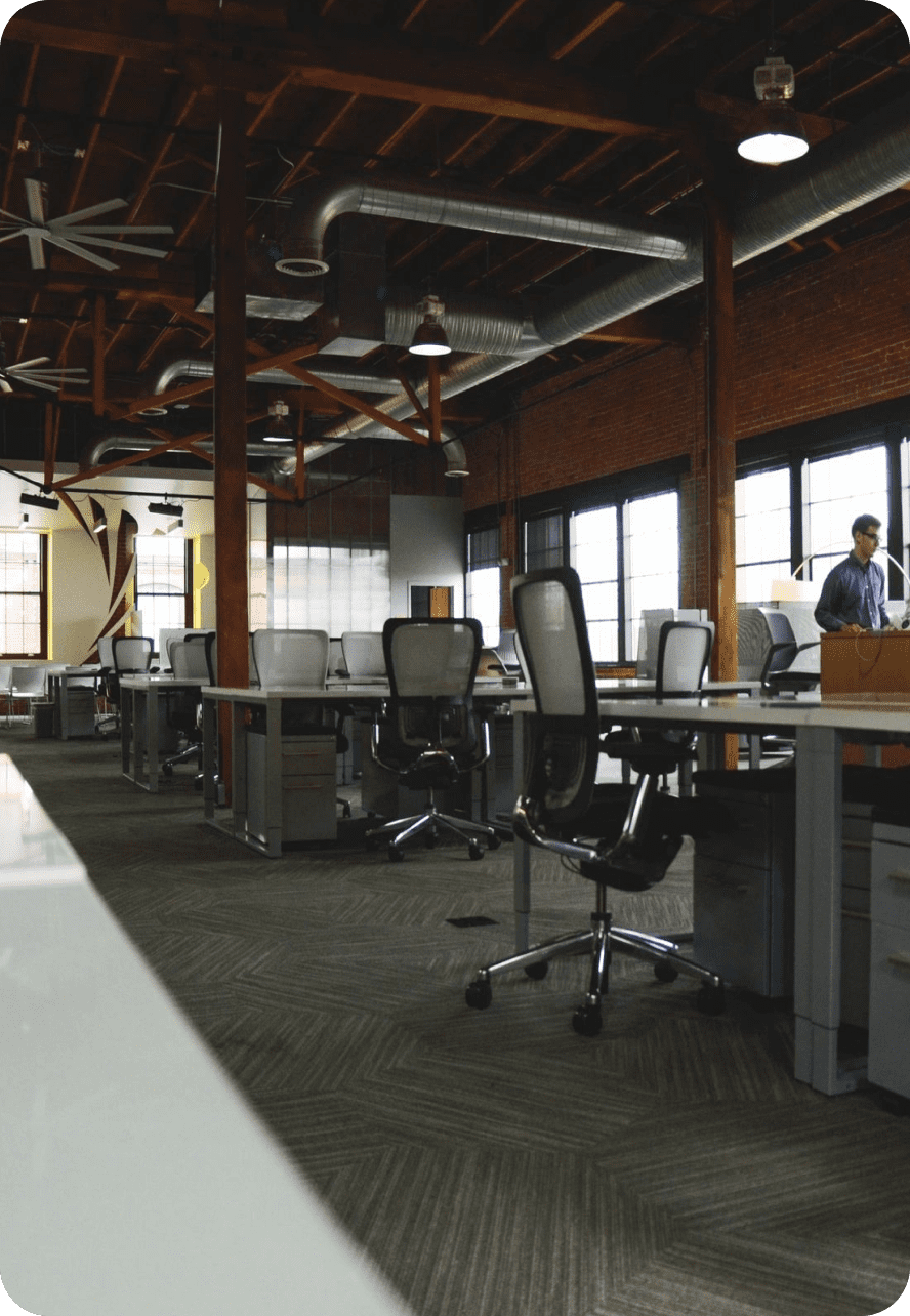 Modern office space with multiple workstations and a person standing near a window.