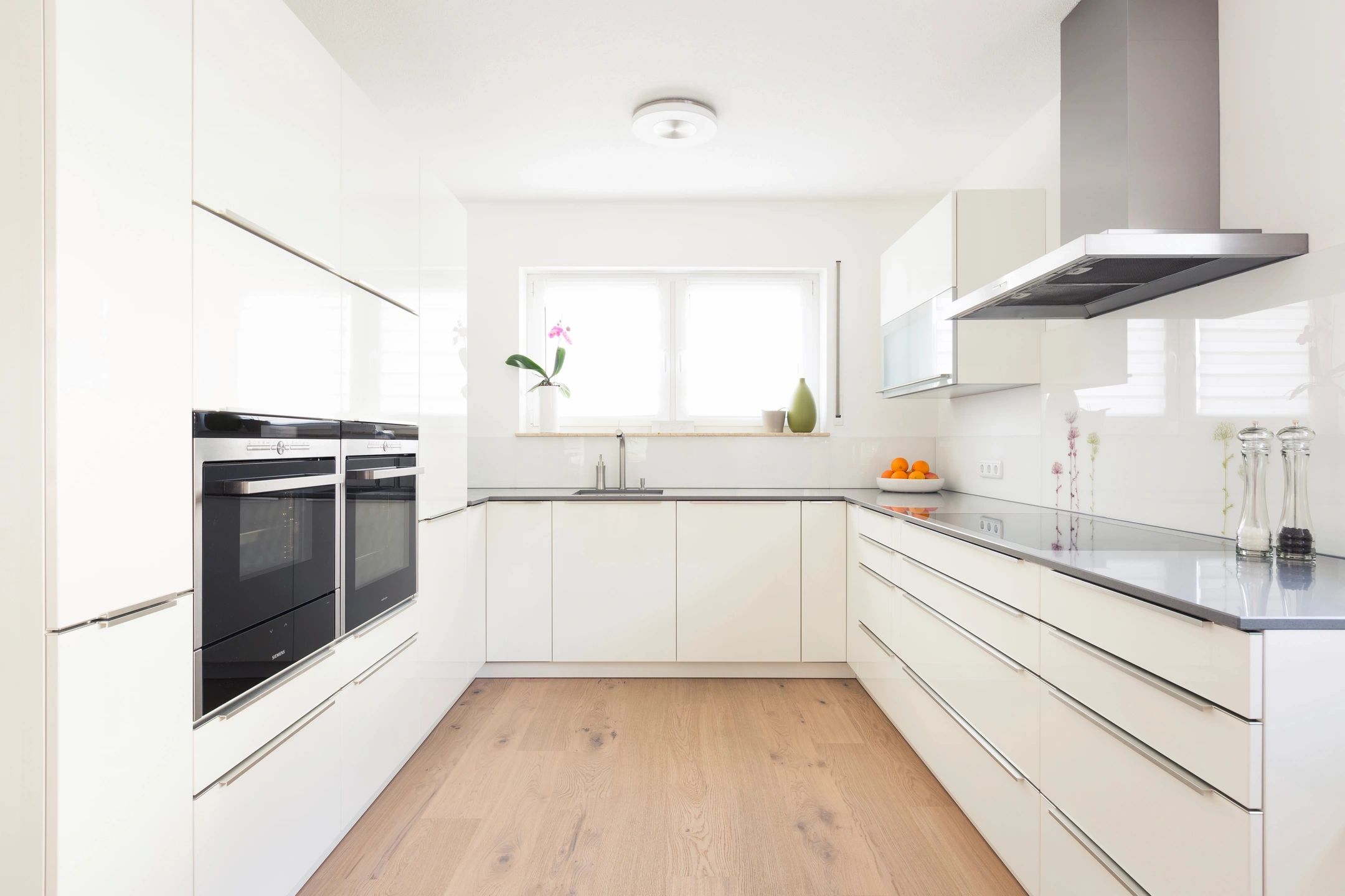 Bright modern kitchen with white cabinets and wooden floor.